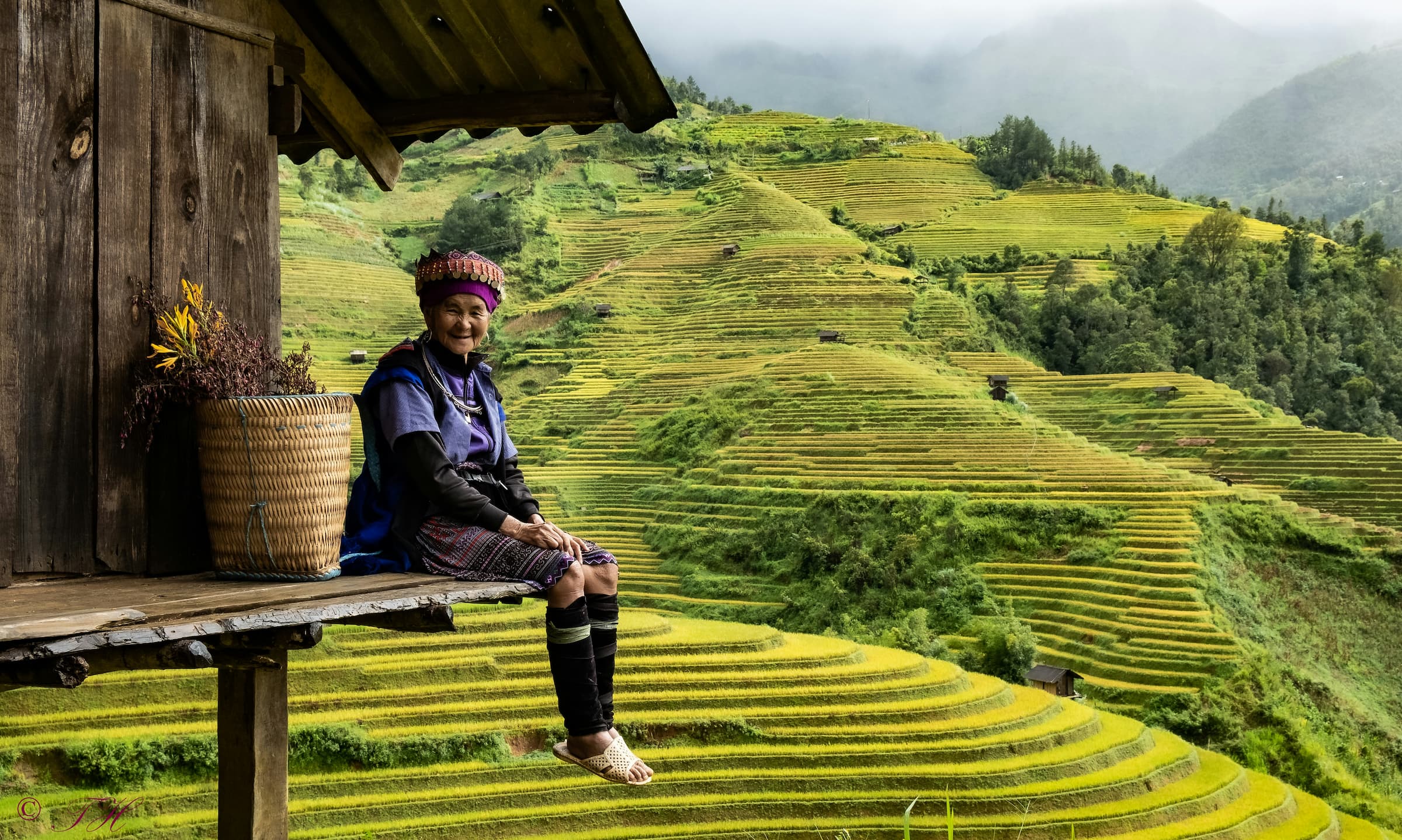 Vietnamese woman smiling while sitting outside her house with fields in the background