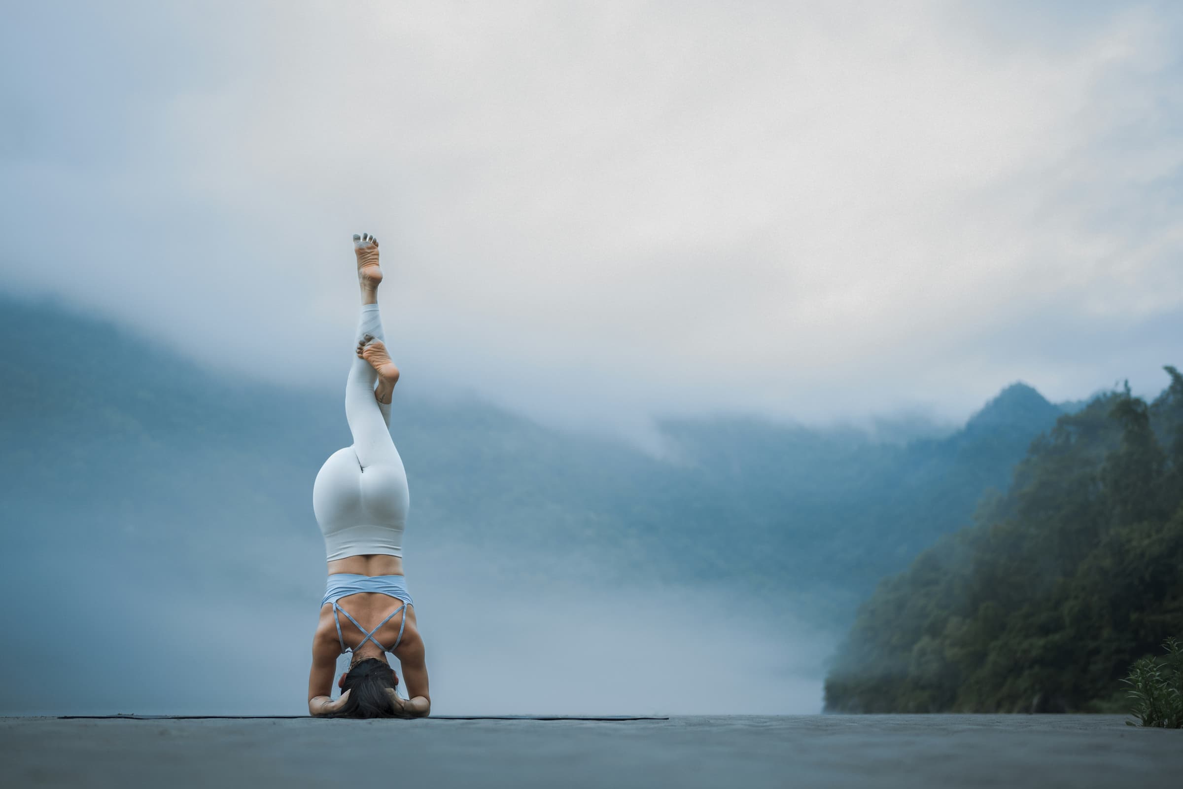 woman practicing headstand outdoors with low clouds